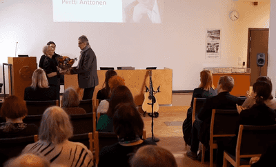 Yleisö taputtaa, kun kukkakimppu ja palkinto ojennetaan Pertti Anttoselle.